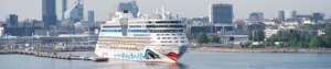 Ein AIDA Kreuzfahrtschiff liegt im Hafen an der Pier in einer großen Stadt.