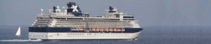 Kreuzfahrtschiff auf See mit Land in Sicht, im Hintergrund kreuzt ein Segelboot